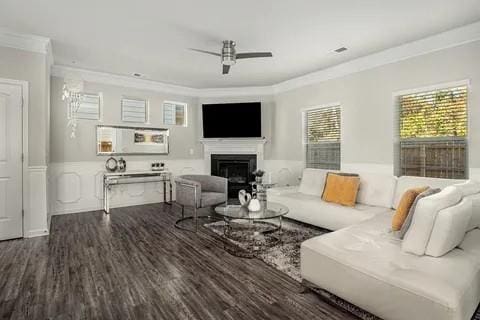 living room with a fireplace, crown molding, wainscoting, ceiling fan, and wood finished floors