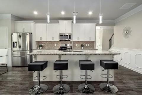 kitchen with appliances with stainless steel finishes, white cabinets, decorative light fixtures, and an island with sink