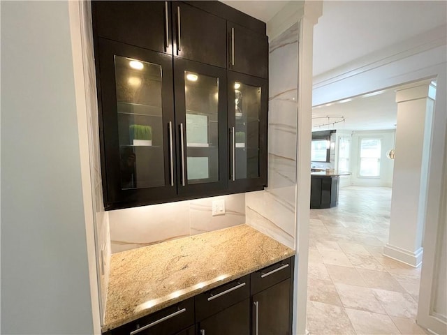 bar featuring dark brown cabinets, light stone countertops, ornamental molding, and ornate columns