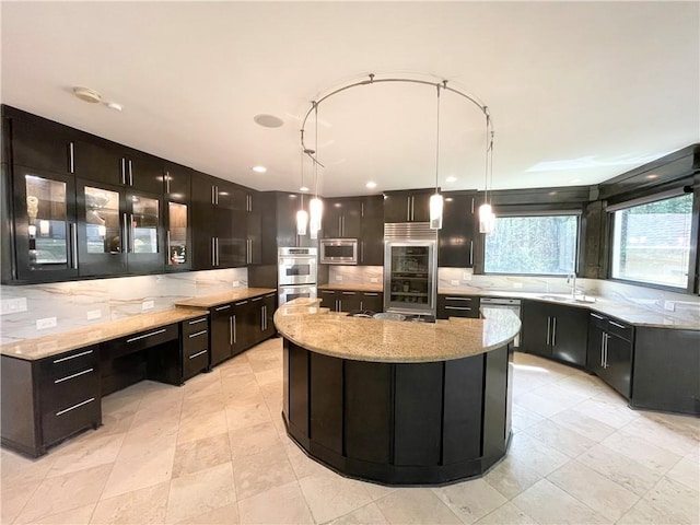 kitchen featuring a spacious island, sink, light stone countertops, decorative light fixtures, and stainless steel appliances