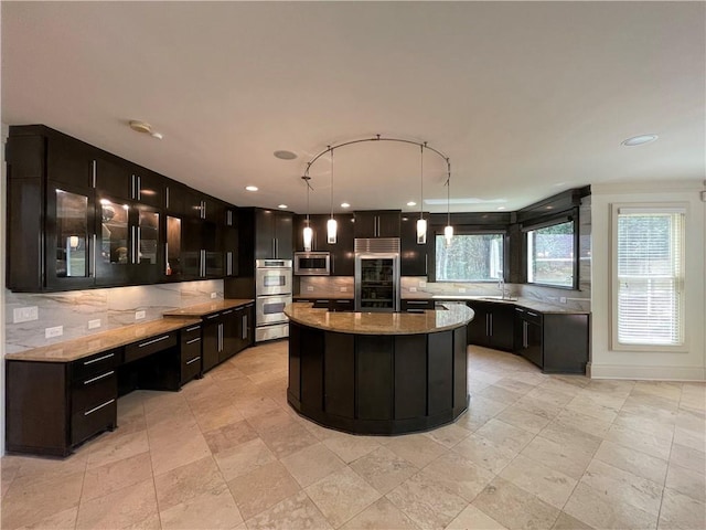 kitchen with light stone countertops, appliances with stainless steel finishes, sink, decorative light fixtures, and a center island