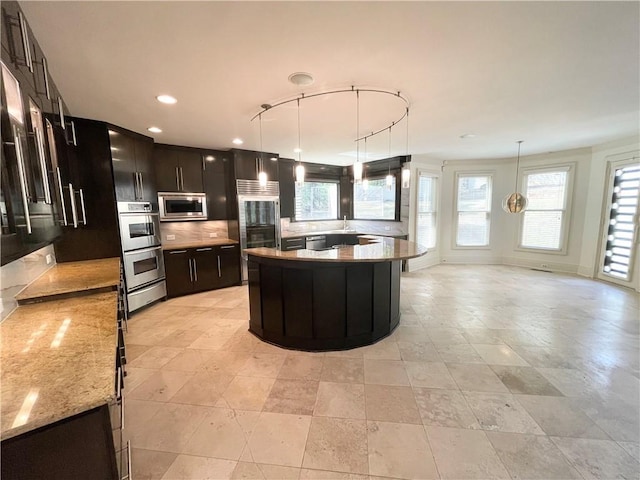 kitchen featuring light stone countertops, tasteful backsplash, built in appliances, decorative light fixtures, and a kitchen island