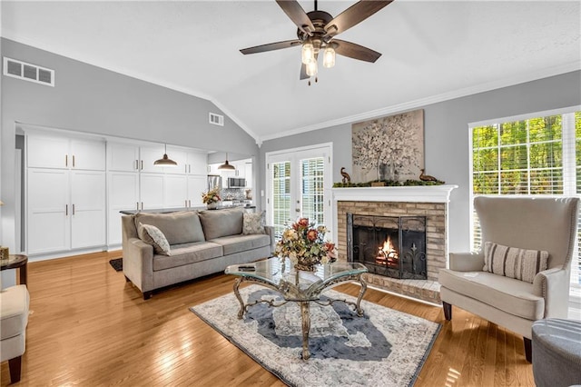 living area featuring ceiling fan, ornamental molding, visible vents, a brick fireplace, and lofted ceiling