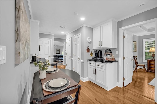 kitchen with light wood-style flooring, white cabinetry, crown molding, and visible vents