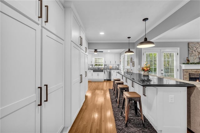 kitchen featuring tasteful backsplash, a kitchen breakfast bar, white cabinets, light wood finished floors, and dishwasher