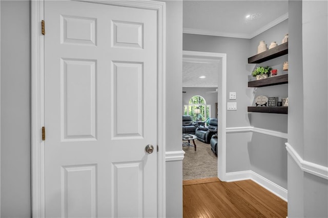 hall with wood finished floors, baseboards, and ornamental molding