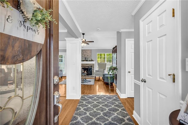 foyer entrance with a fireplace, a textured ceiling, ornamental molding, a ceiling fan, and wood finished floors