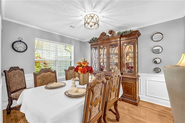 dining area featuring crown molding, visible vents, a wainscoted wall, light wood finished floors, and a notable chandelier