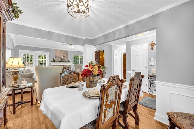 dining space featuring a fireplace, light wood-style flooring, ornate columns, and ornamental molding