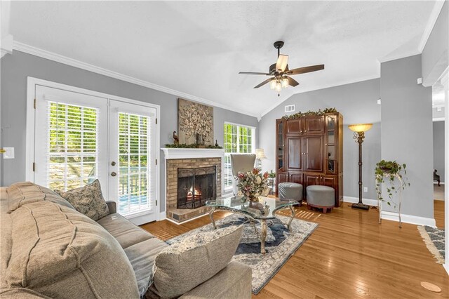living room with a lit fireplace, light wood-type flooring, a ceiling fan, ornamental molding, and baseboards