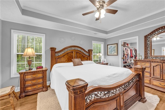 bedroom featuring a raised ceiling, a closet, light wood finished floors, and a walk in closet