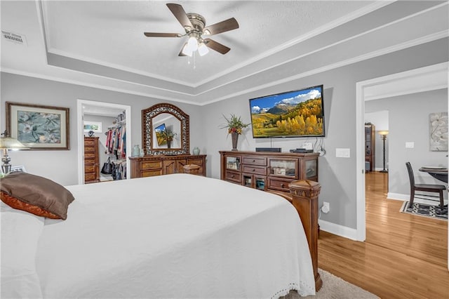 bedroom with crown molding, visible vents, a raised ceiling, and wood finished floors