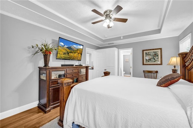 bedroom with a raised ceiling, ceiling fan, baseboards, and light wood-style flooring