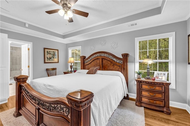 bedroom with light wood-style flooring, crown molding, connected bathroom, visible vents, and a raised ceiling