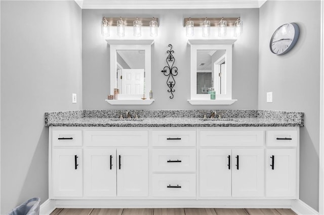 bathroom with crown molding, double vanity, a sink, and baseboards