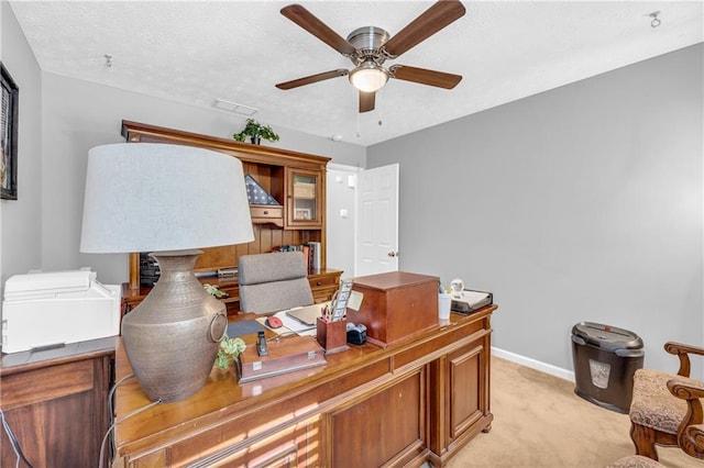 home office featuring baseboards, a textured ceiling, visible vents, ceiling fan, and light colored carpet