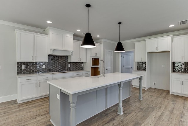 kitchen featuring sink, decorative light fixtures, an island with sink, white cabinetry, and black stovetop