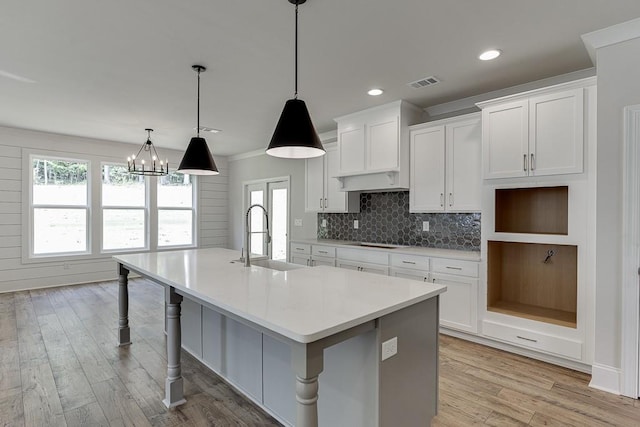 kitchen with pendant lighting, a kitchen island with sink, white cabinets, sink, and stovetop