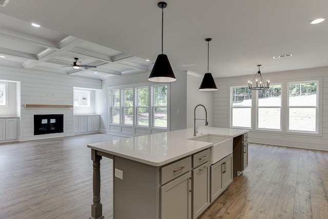 kitchen featuring a kitchen island with sink, coffered ceiling, hanging light fixtures, a fireplace, and beam ceiling