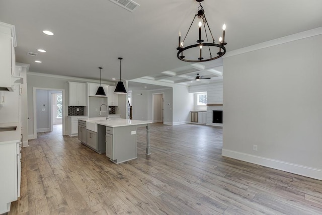 kitchen featuring hanging light fixtures, coffered ceiling, beamed ceiling, an island with sink, and a fireplace