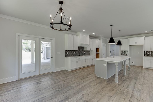 kitchen featuring white cabinets, a kitchen island with sink, hanging light fixtures, and tasteful backsplash