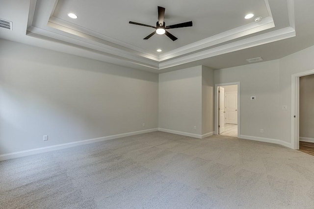 spare room featuring light carpet, a tray ceiling, and ceiling fan