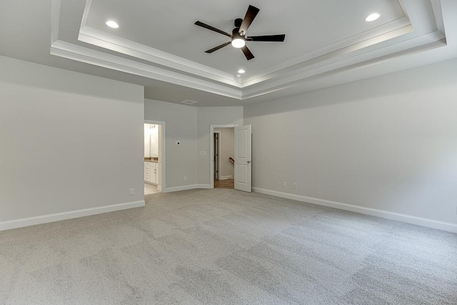 unfurnished bedroom with a tray ceiling, connected bathroom, ceiling fan, and light colored carpet