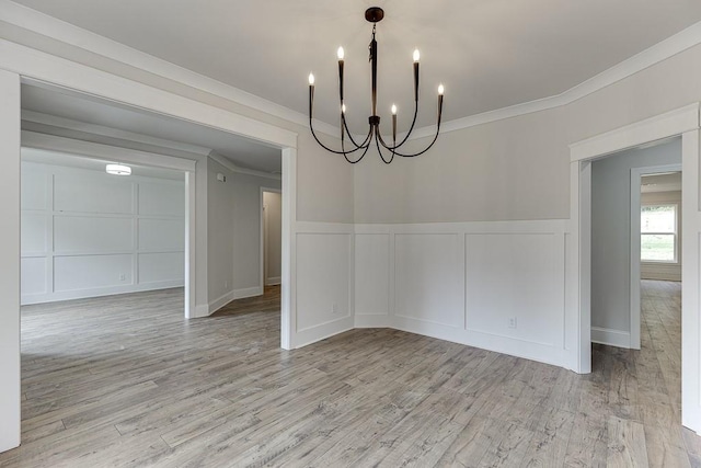 unfurnished dining area featuring light wood-type flooring, crown molding, and a chandelier