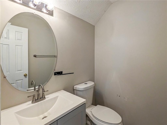 bathroom with toilet, vanity, a textured ceiling, and vaulted ceiling