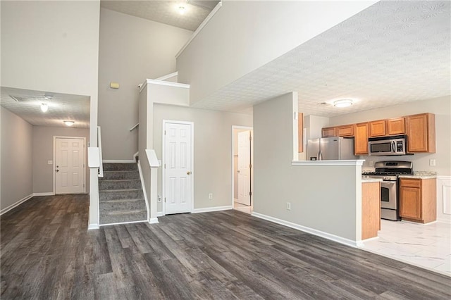 kitchen with appliances with stainless steel finishes, a textured ceiling, dark hardwood / wood-style floors, and a high ceiling