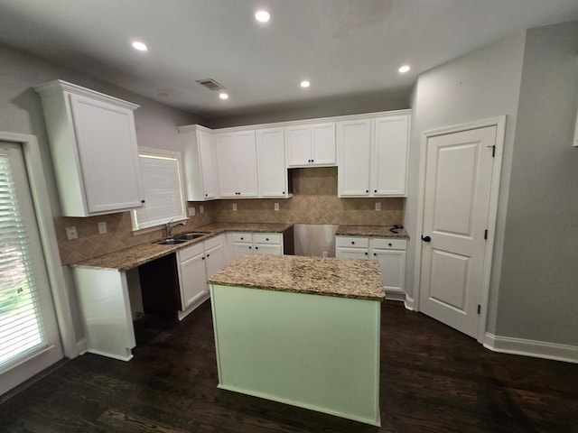 kitchen featuring dark wood-type flooring, sink, light stone counters, a kitchen island, and white cabinets