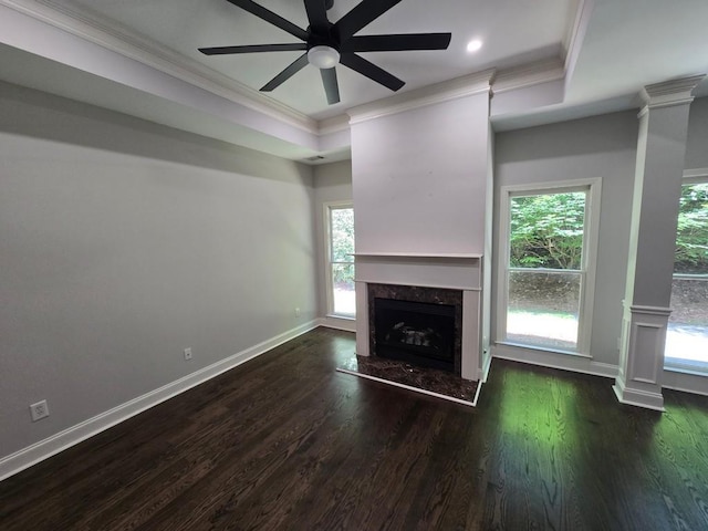 unfurnished living room with a raised ceiling, a healthy amount of sunlight, dark wood-type flooring, and ornate columns