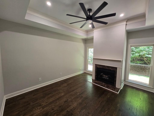 unfurnished living room featuring dark wood-type flooring, crown molding, a raised ceiling, ceiling fan, and a fireplace