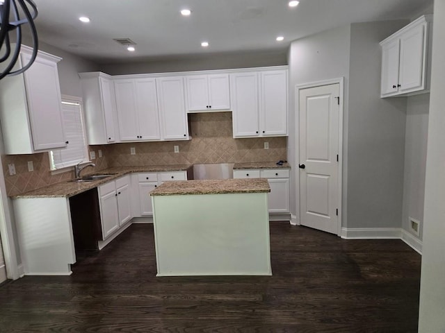 kitchen featuring light stone countertops, a kitchen island, sink, and white cabinets