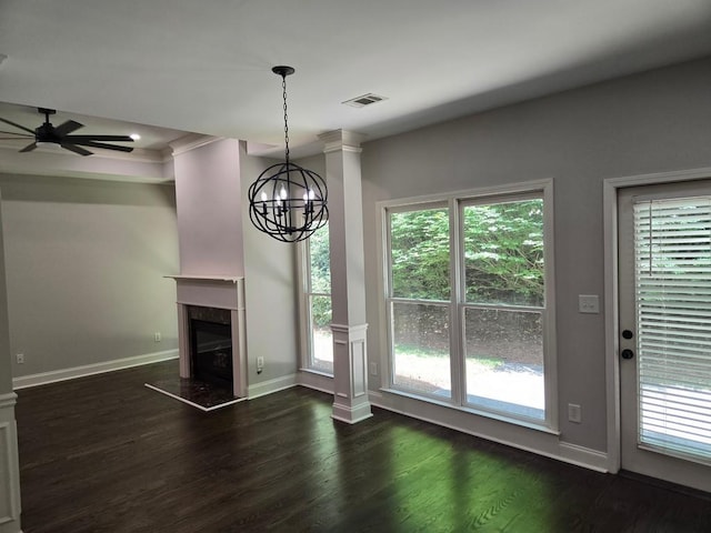 unfurnished living room with dark wood-type flooring, ceiling fan with notable chandelier, decorative columns, and crown molding