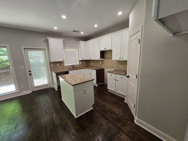 kitchen featuring a kitchen island, tasteful backsplash, white cabinetry, dark hardwood / wood-style flooring, and light stone counters