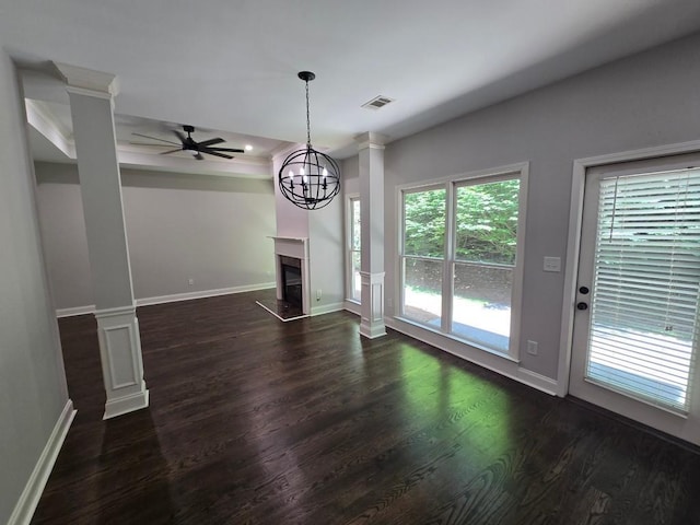 unfurnished living room with ornate columns, ceiling fan with notable chandelier, and dark hardwood / wood-style flooring