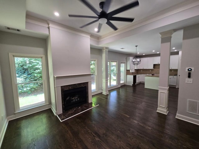 unfurnished living room with ornate columns, a tray ceiling, dark hardwood / wood-style floors, a fireplace, and ceiling fan with notable chandelier