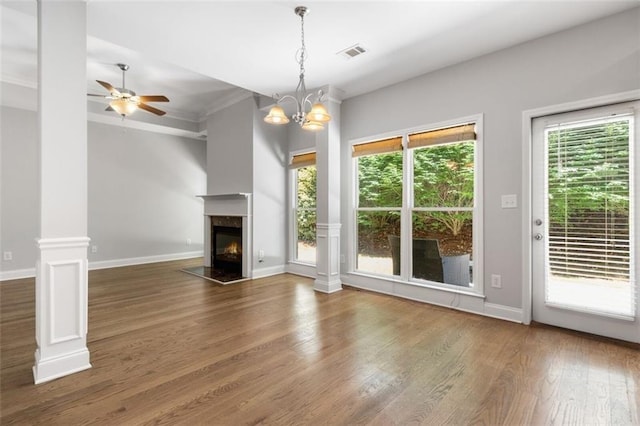 unfurnished living room featuring ornate columns, ceiling fan with notable chandelier, a fireplace, ornamental molding, and dark wood-type flooring