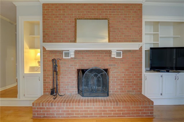 unfurnished living room featuring crown molding, a brick fireplace, light hardwood / wood-style floors, and built in shelves