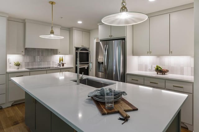 kitchen with appliances with stainless steel finishes, an island with sink, a sink, and tasteful backsplash