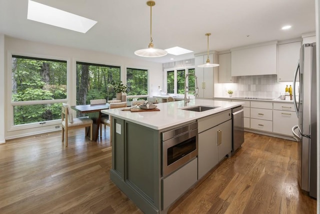 kitchen with a kitchen island with sink, a skylight, appliances with stainless steel finishes, and a sink