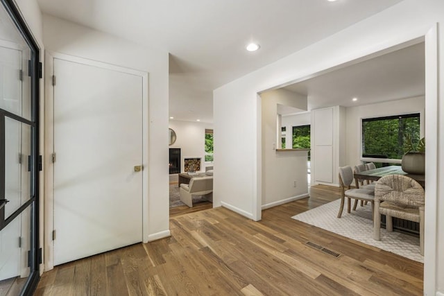 entryway featuring visible vents, wood finished floors, baseboards, a warm lit fireplace, and recessed lighting