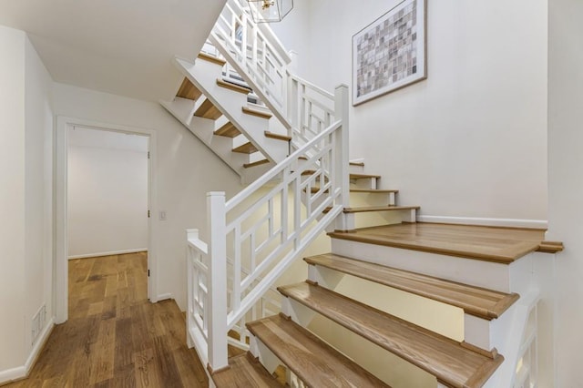 staircase with baseboards, wood finished floors, and visible vents