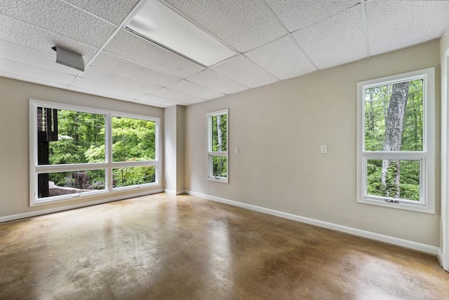 empty room featuring baseboards, plenty of natural light, concrete flooring, and a drop ceiling