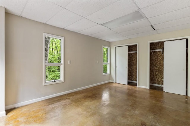 unfurnished bedroom featuring multiple closets, multiple windows, concrete floors, and a paneled ceiling
