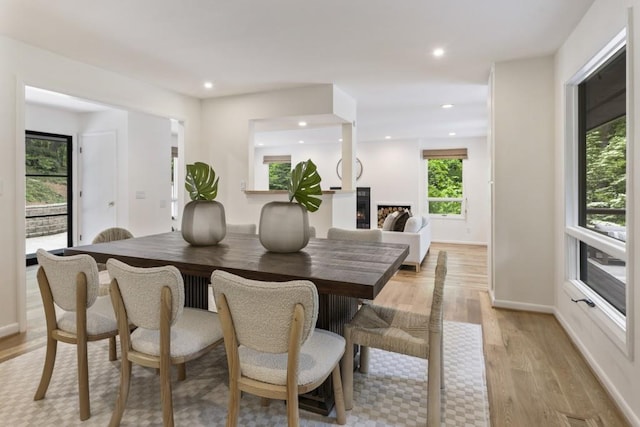 dining area with recessed lighting, baseboards, a lit fireplace, and light wood-style flooring