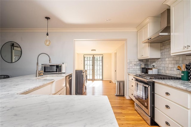 kitchen with decorative backsplash, appliances with stainless steel finishes, french doors, light wood-style floors, and wall chimney exhaust hood