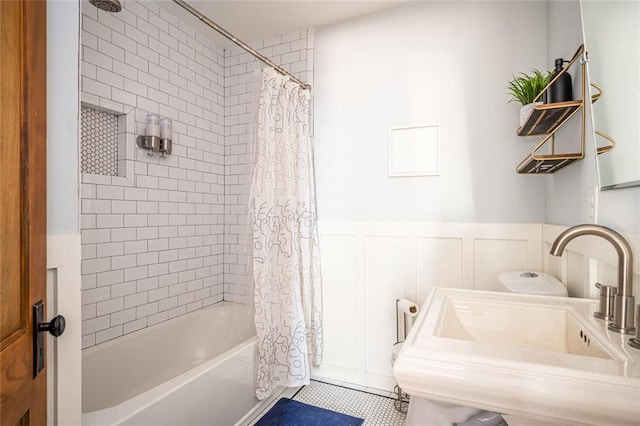 full bath featuring shower / bathtub combination with curtain, a sink, wainscoting, a decorative wall, and tile patterned flooring