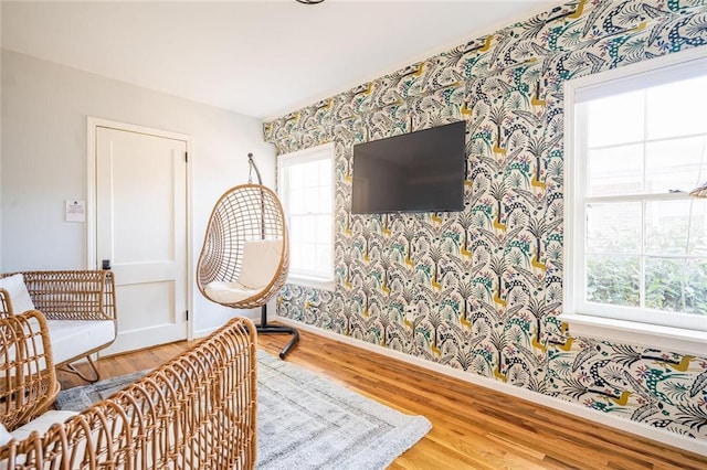 living area featuring wallpapered walls, baseboards, and wood finished floors